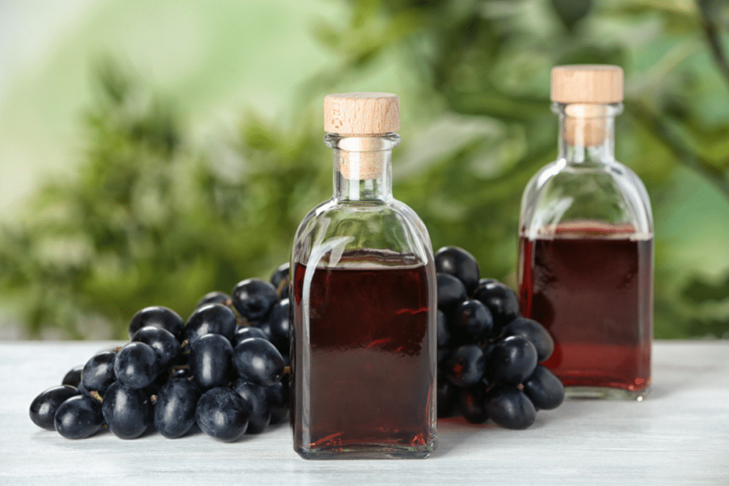 sticle cu otet de vin si struguri pe masa din lemn